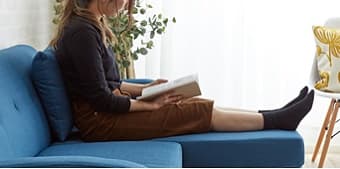 ブルーのカウチソファのフットスツールに足を預けて読書する女性