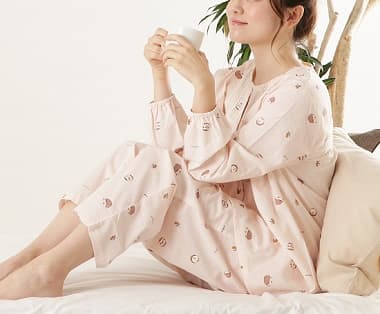 長袖コットンパジャマ　ピンクを着てベッドの上でコーヒーを飲んでリラックスする女性