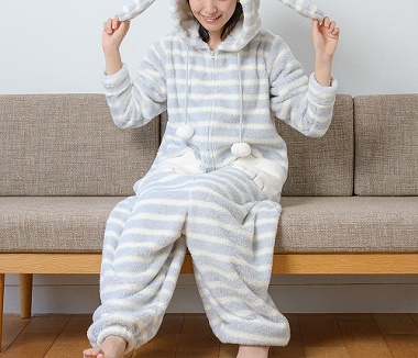 グレーのボーダーのウサギ着ぐるみパジャマを着てフードをかぶりソファに座る女性